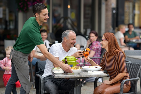 Der Kellner bringt das Mittagessen an einen Tisch, an dem ein älterer Mann und eine Frau einen Toast ausbringen