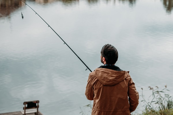 Ein Mann mit brauner Jacke angelt am ruhigen Wasser.