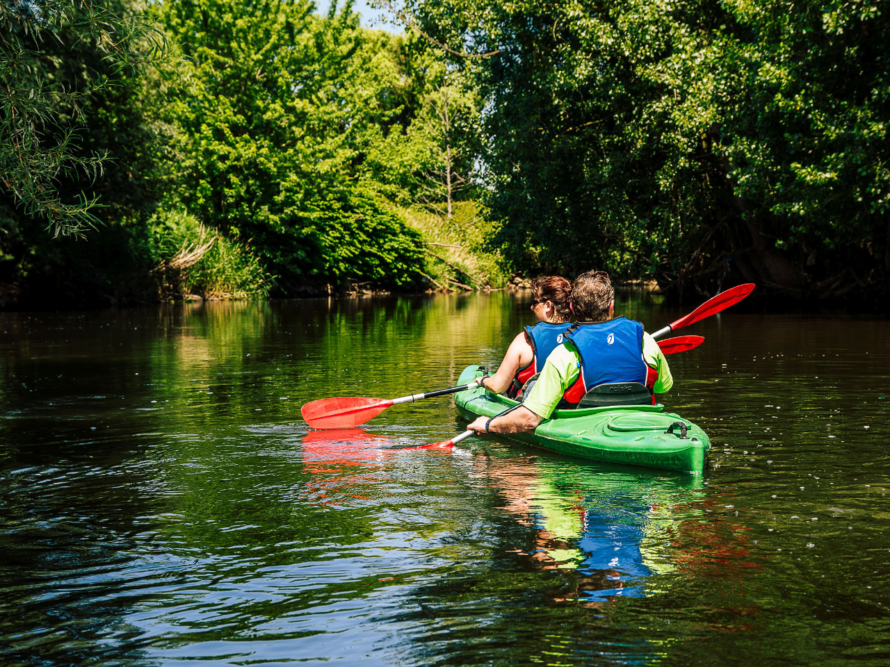 Twee mensen zitten in een kano en varen over de Roer in de gemeente Roerdalen