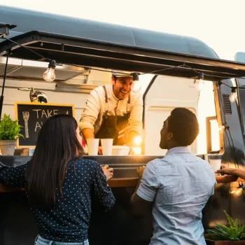 Twee mensen bestellen eten bij een vrolijke foodtruckkok tijdens een zomerse avond.