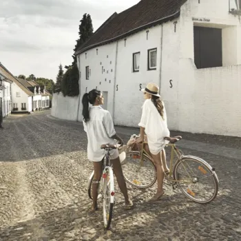 Zwei Frauen mit Fahrrädern stehen auf einem Kopfsteinpflasterweg im weißen Städtchen Thorn.