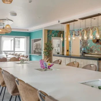 Gezellige groepsruimte met lange tafel, kleurrijke wanddecoratie en moderne verlichting.