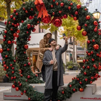 Twee mensen maken een selfie in een grote kerstkrans met rode ballen tijdens de Christmas Sale in Designer Outlet Roermond.